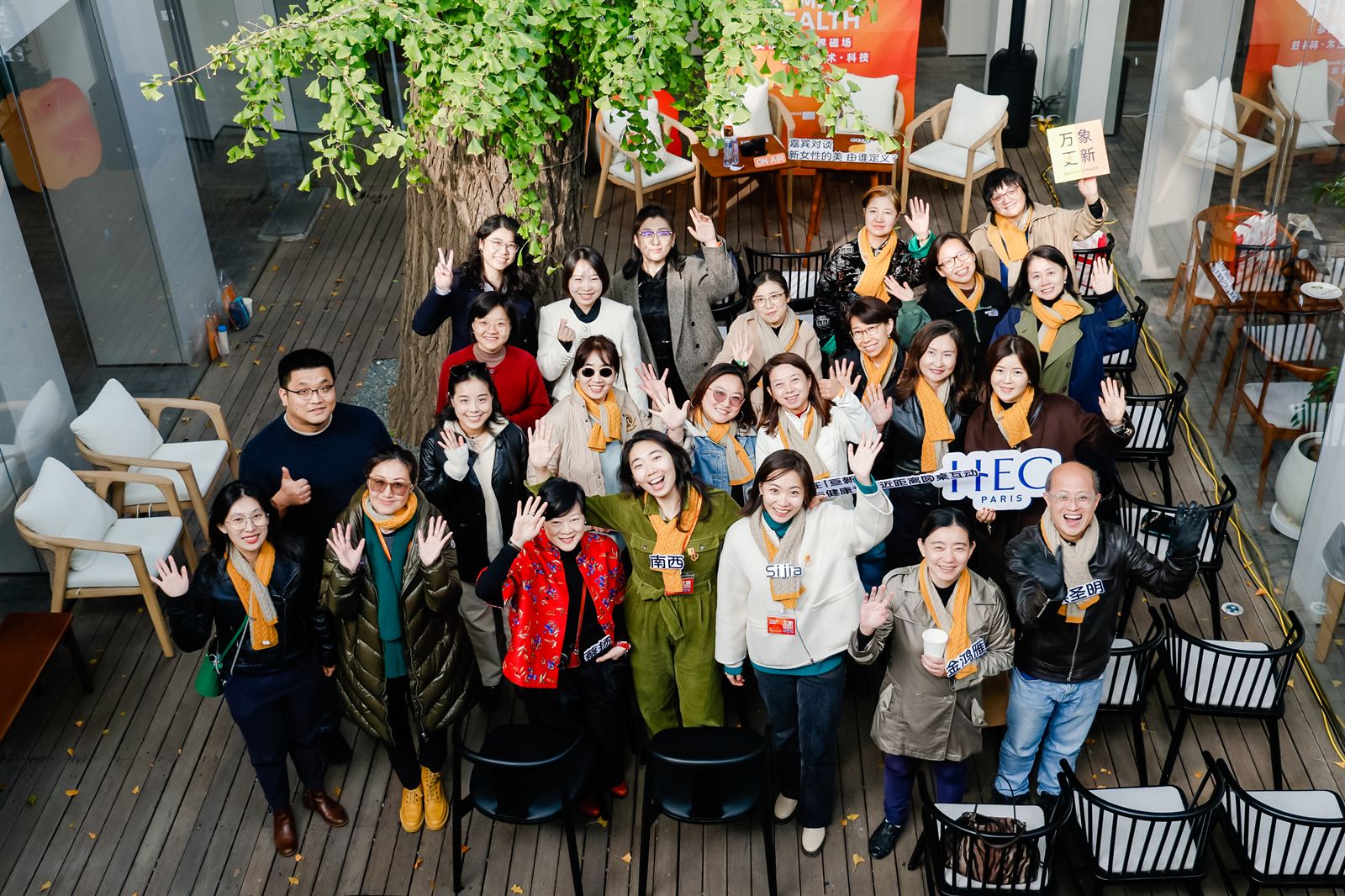A large group in the ginkgo courtyard at 亘新, photographed from above, one attendee holding an HEC Paris sign